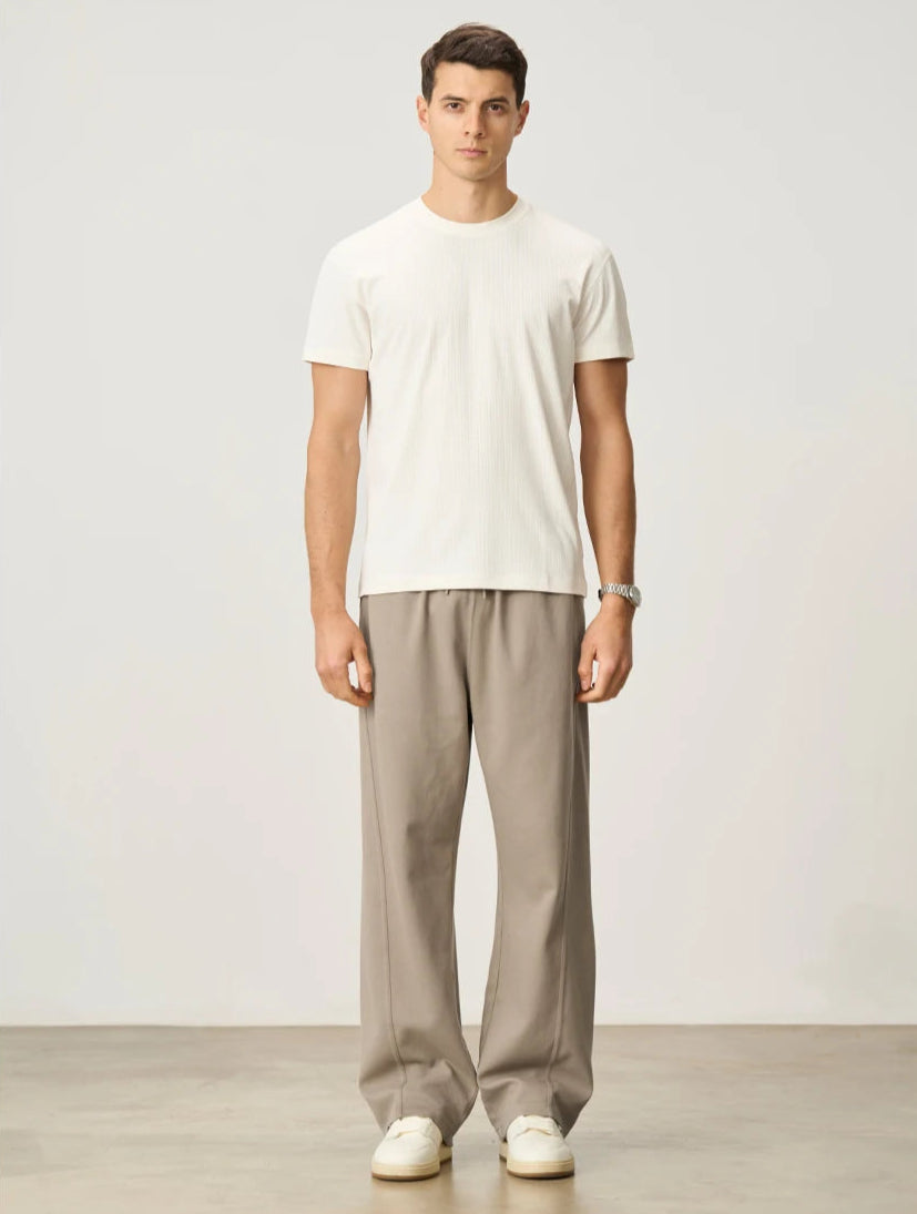 CIIVET - Model wearing a white t-shirt and beige pants standing against a plain background
